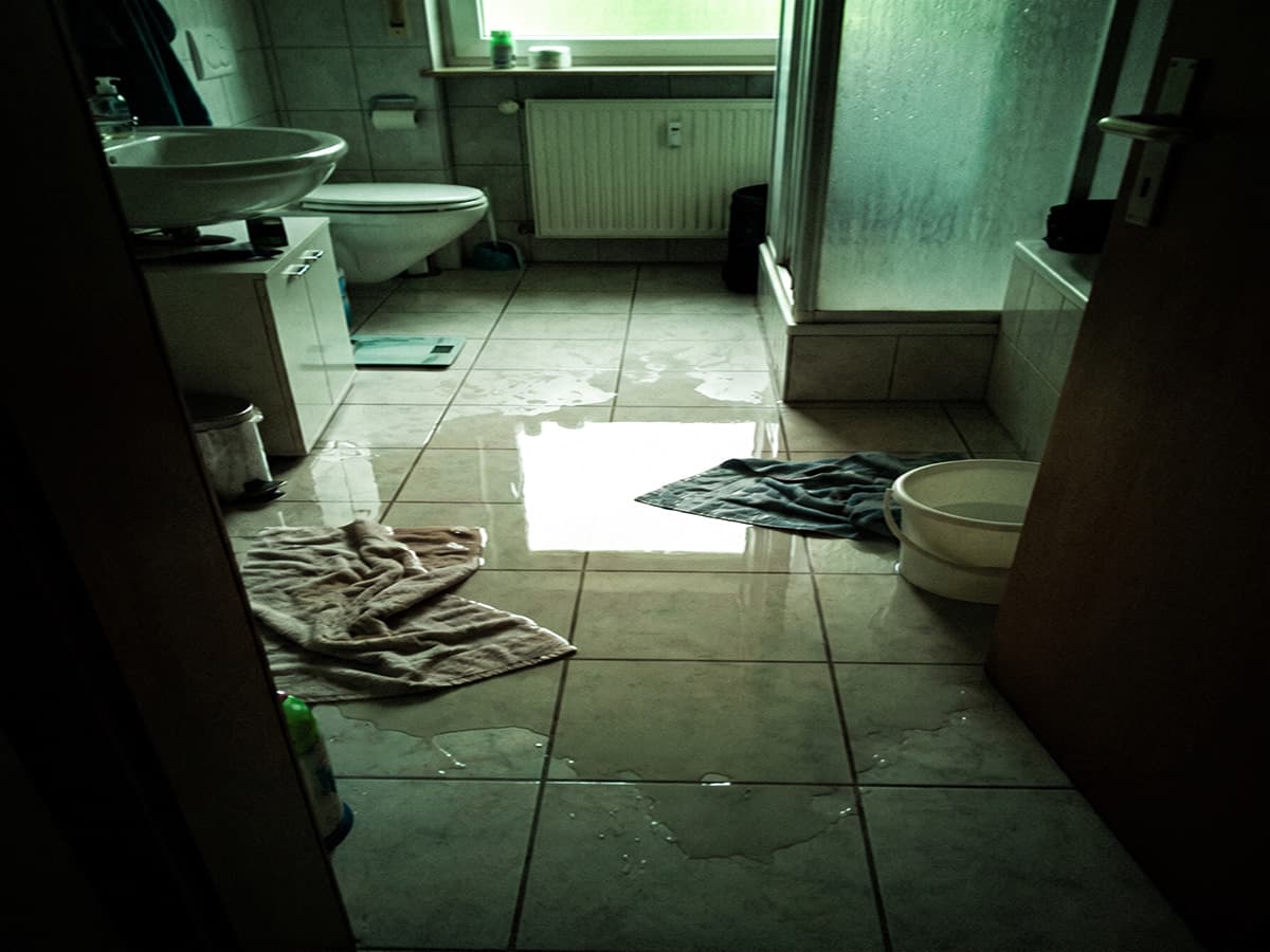 Handyfoto eines Kunden: Wasserpfütze auf dem Badezimmerboden vor dem Waschbeckenunterschrank, KI-generiertes Beispielbild