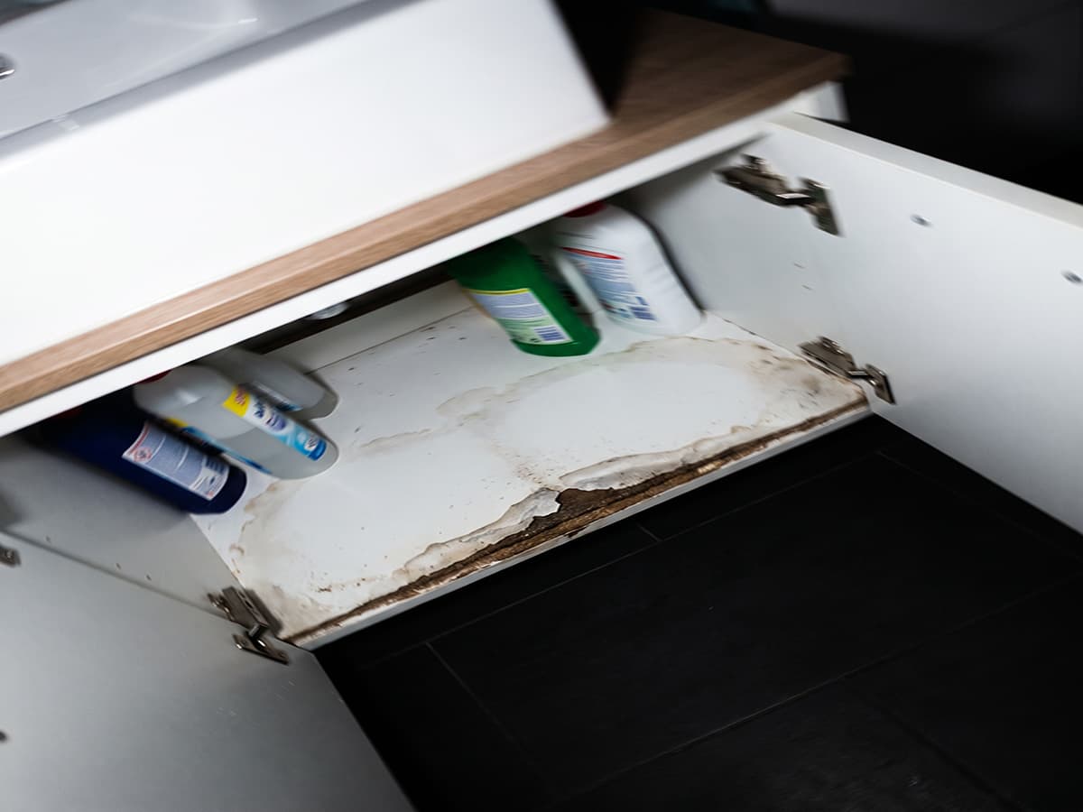 Handyfoto eines Kunden: durch Wasser aufgequollene Spanplatte im Waschbeckenunterschrank, KI-generiertes Beispielbild